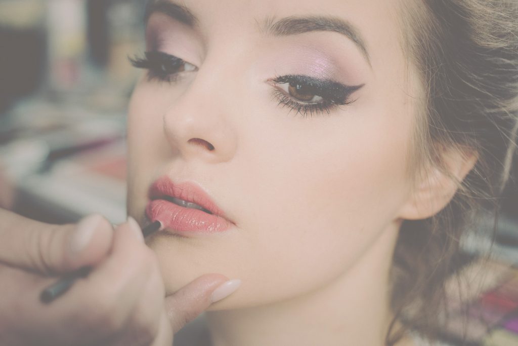 Een vrouw krijgt make-up aangebracht op haar lippen.